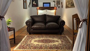 A living room with a brown leather sofa, a patterned rug, a ceiling fan, and a television on a wooden stand. - Goblin's Inn (St. Helena Bay)