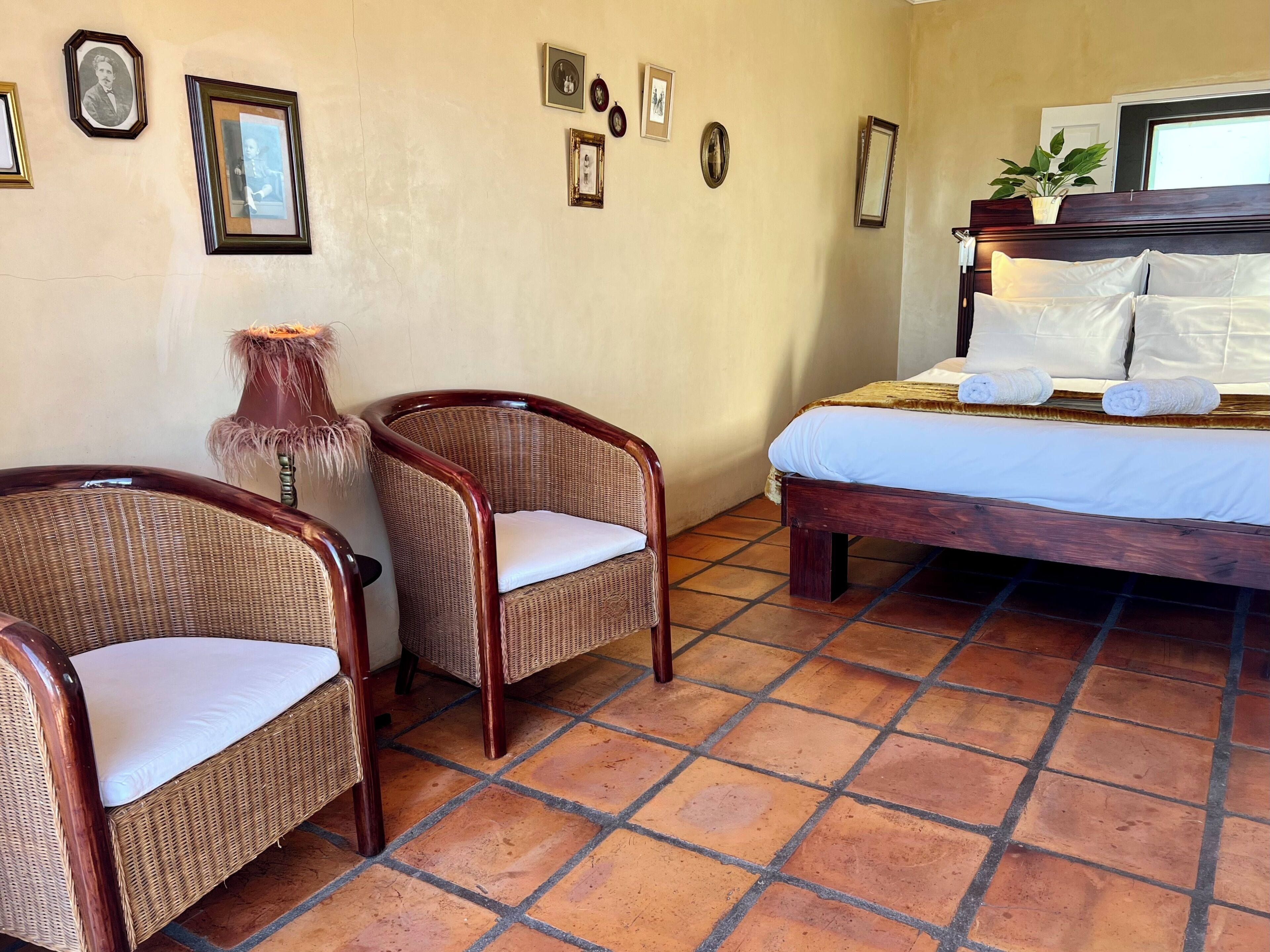 A hotel room with a bed, two wicker chairs, a small table, and several framed pictures on the wall.
