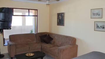 Sala de estar com um sofá marrom, uma mesa de centro e um ventilador de teto. Há quadros nas paredes.