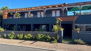A two-story building with a dark facade, wooden balconies, and a covered entrance area. - Goblin's Inn (St. Helena Bay)