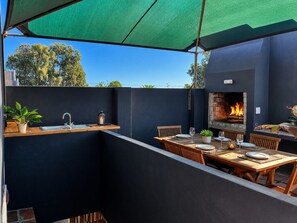 An outdoor patio with a dining table, chairs, a built-in grill, and a sink.