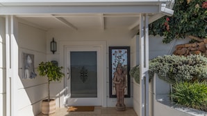 A white exterior with a door, a potted plant, a statue, and a stone wall with greenery. - Port Of Call (Cape Town)