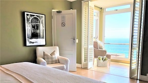 A bedroom with a bed, a chair, a door, and a view of the sea through a balcony. - Port Of Call (Cape Town)