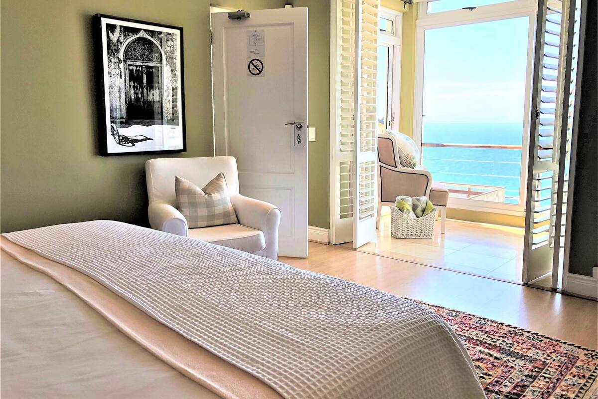 Une chambre à coucher avec un lit, une chaise, une porte et une vue sur la mer depuis un balcon.