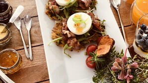 A breakfast tray with a variety of foods including eggs, bacon, and tomatoes, along with glasses of orange juice and a dessert. - Port Of Call (Cape Town)