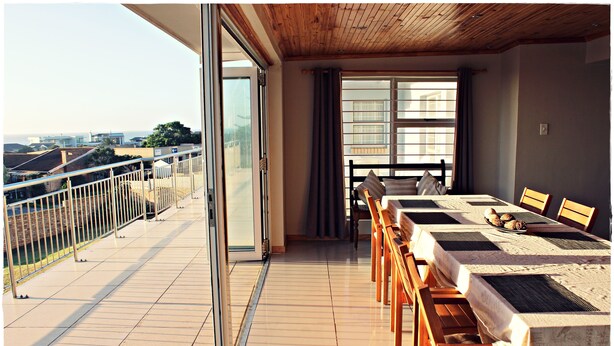A balcony with a view of the sea, a dining area with tables and chairs, and a wooden ceiling. - Madiolyn (Jeffreys Bay)