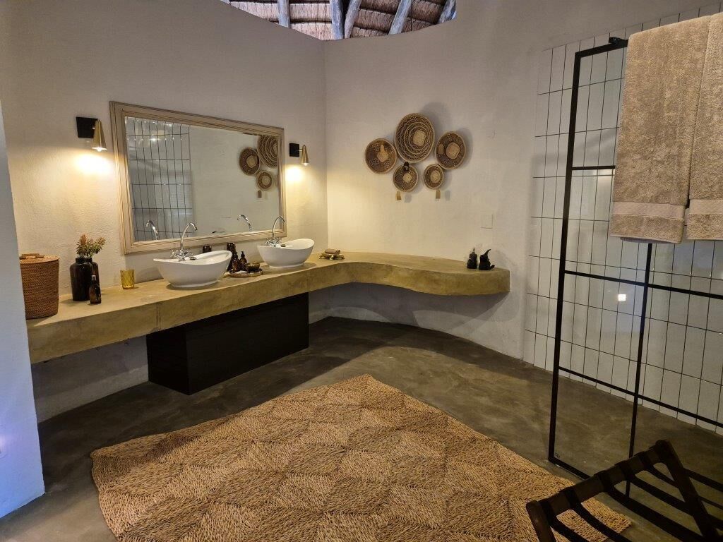 A modern bathroom with a curved vanity, two sinks, a large mirror, and a shower area.
