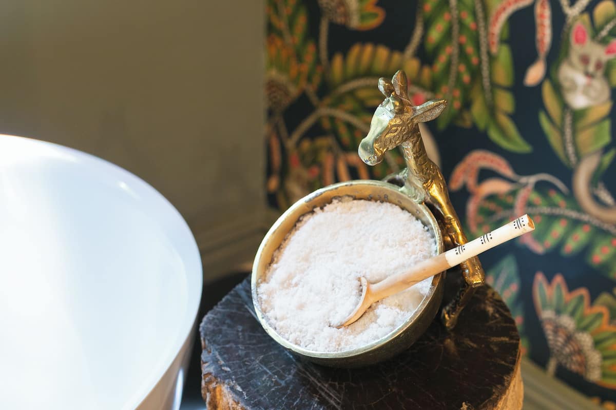 A bowl of salt with a spoon on a wooden surface, a decorative horse figurine, and a white bathtub.