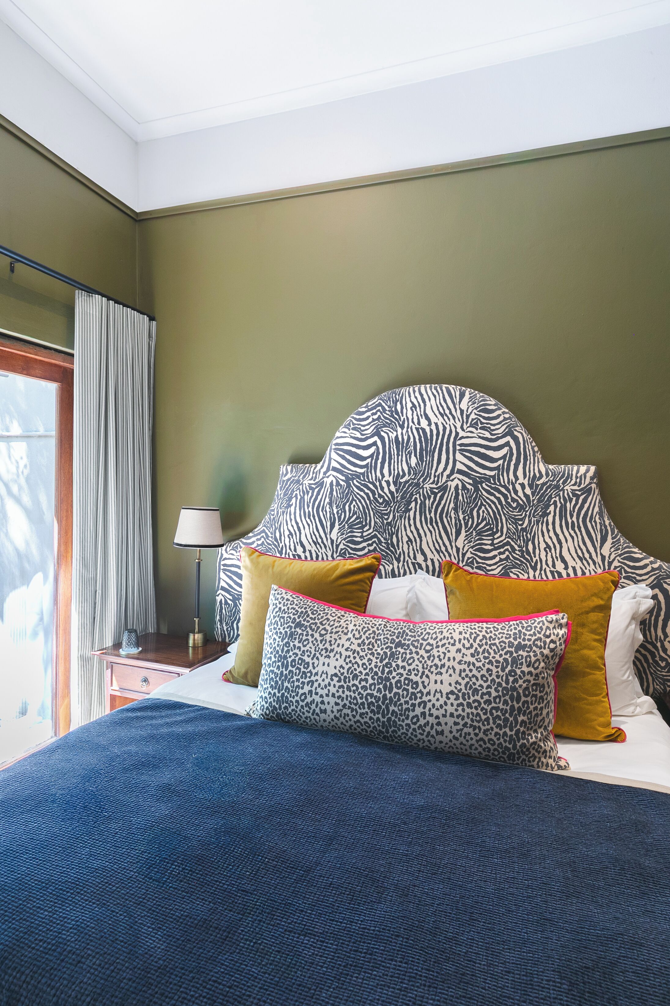 Un dormitorio con cabecera de estampado de cebra, cama con cubrecama azul y mesita de noche con lámpara.