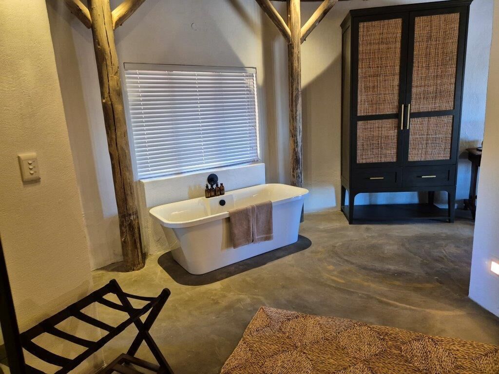 A bathroom with a freestanding bathtub, a wooden chair, and a woven rug.