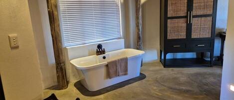 A bathroom with a freestanding bathtub, a wooden chair, and a woven rug.
