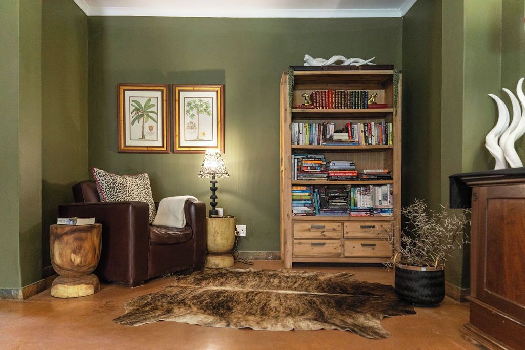 A cozy living room with a leather armchair, a wooden bookshelf, framed pictures, and a fur rug.