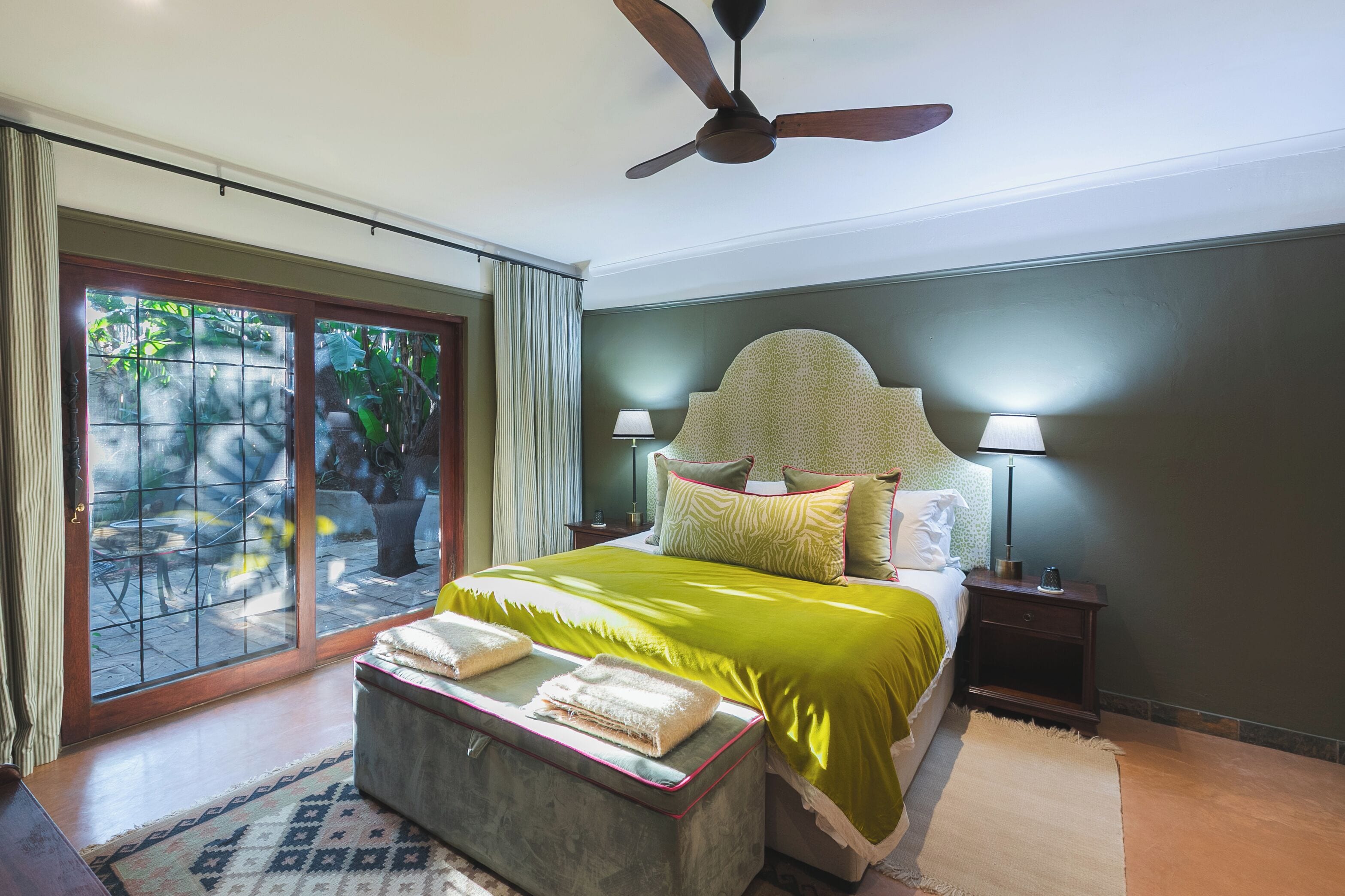 A bedroom with a bed, a ceiling fan, a nightstand, a lamp, and a view through a glass door.