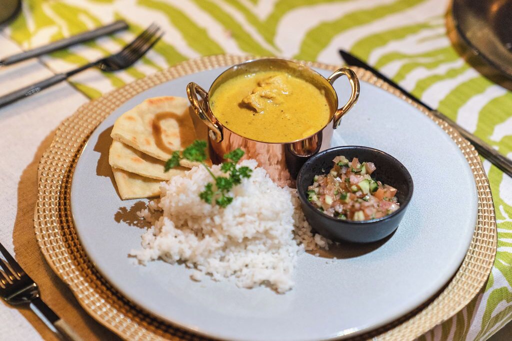 Un plato de arroz blanco, un tazón de curry, un pequeño tazón de ensalada y pan plano sobre una mesa con mantel estampado.