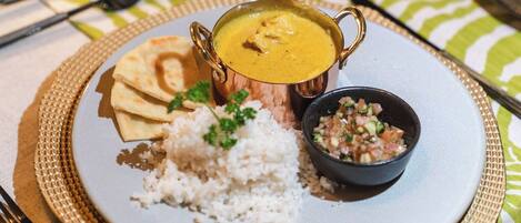 Un plato de arroz blanco, un tazón de curry, un pequeño tazón de ensalada y pan plano sobre una mesa con mantel estampado.