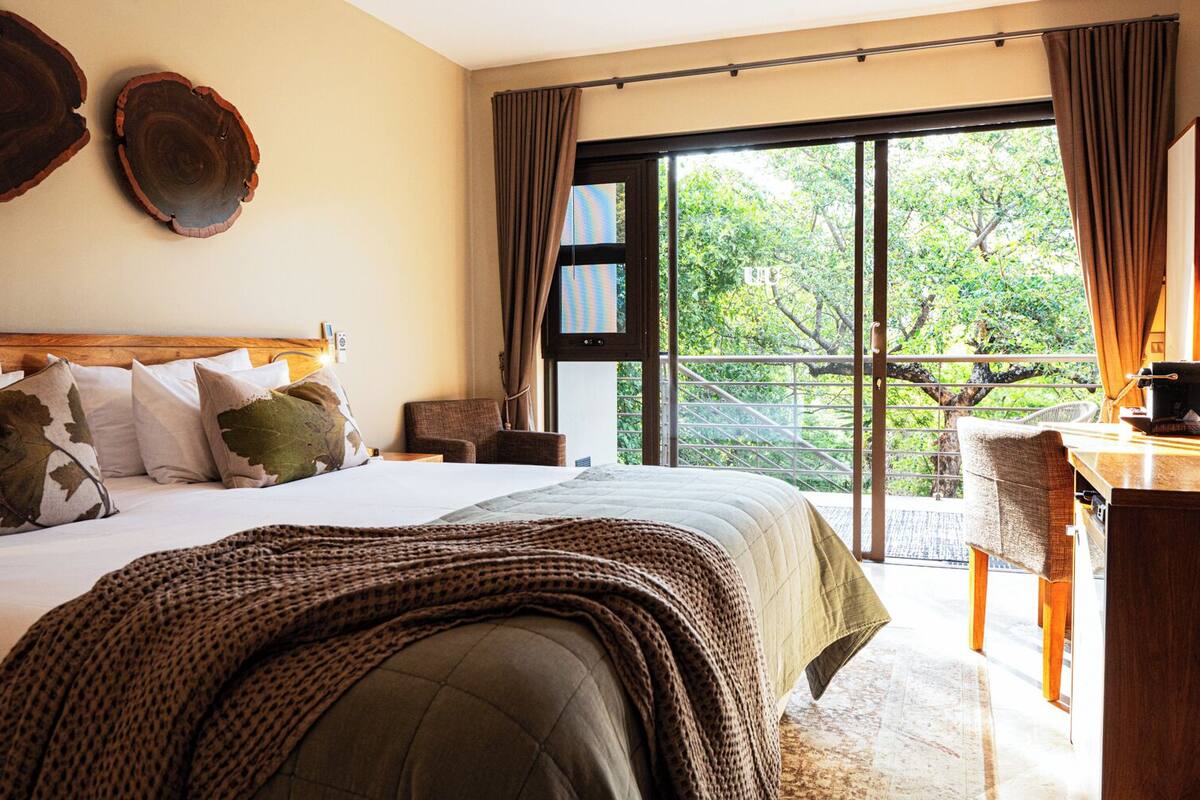 A bedroom with a large bed, a desk, and a view of greenery outside.