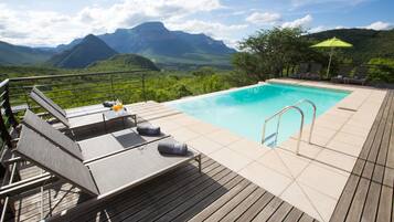 A pool with a wooden deck, lounge chairs, and a view of mountains.