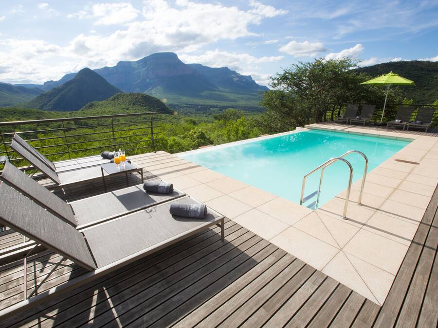 A pool with a wooden deck, lounge chairs, and a view of mountains.