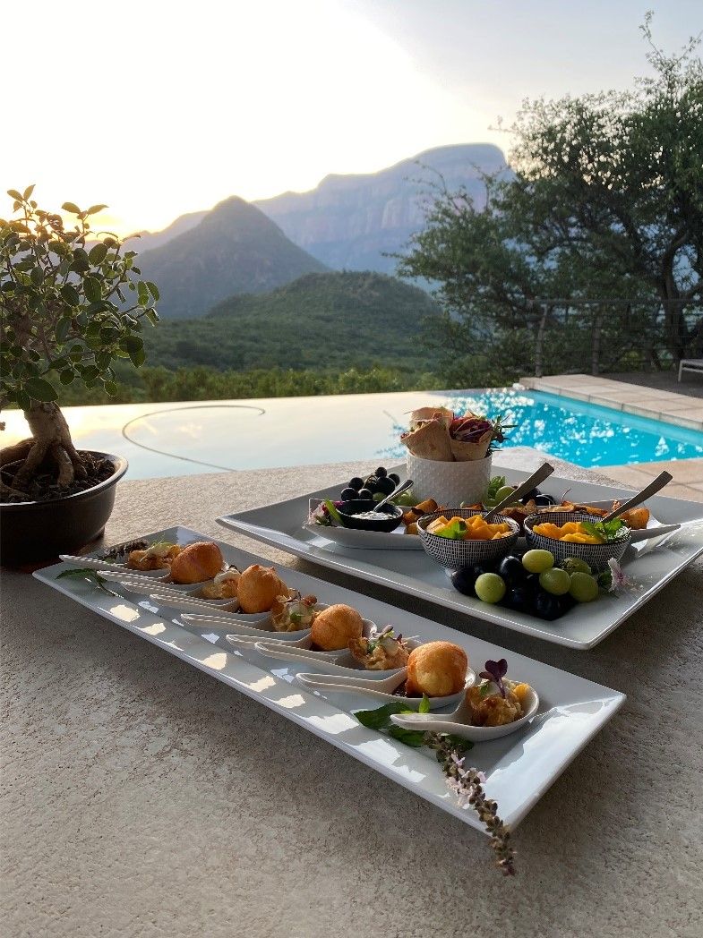 A dining setup with a pool view, including plates of appetizers and a potted plant.