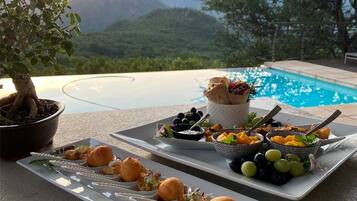 A dining setup with a pool view, including plates of appetizers and a potted plant.
