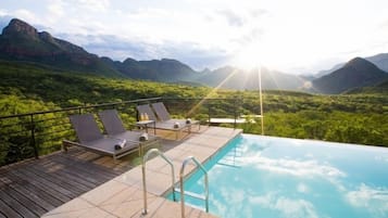 Una piscina al aire libre, sombrillas, sillones reclinables de piscina