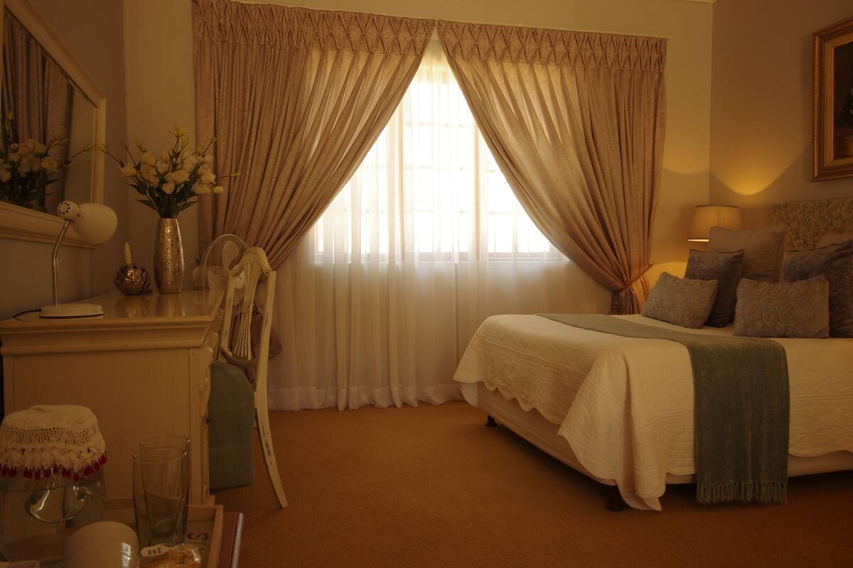 A bedroom with a bed, a dresser, a mirror, and a window with curtains.