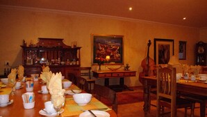 Ein Esszimmer mit einem langen Tisch, gedeckt für eine Mahlzeit, umgeben von Stühlen. Es gibt eine Holzkommode mit Dekorationen und ein Gemälde an der Wand.