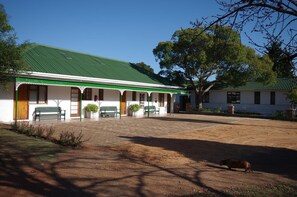 A building with a green roof and white walls, a covered porch with benches, and a dirt courtyard. - Fynbos Guesthouse Riversdale (Riversdale)