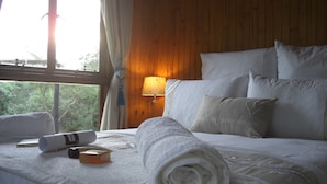 Een net opgemaakt bed met witte lakens en kussens, een opgerolde handdoek en een flesje lotion op het bed.