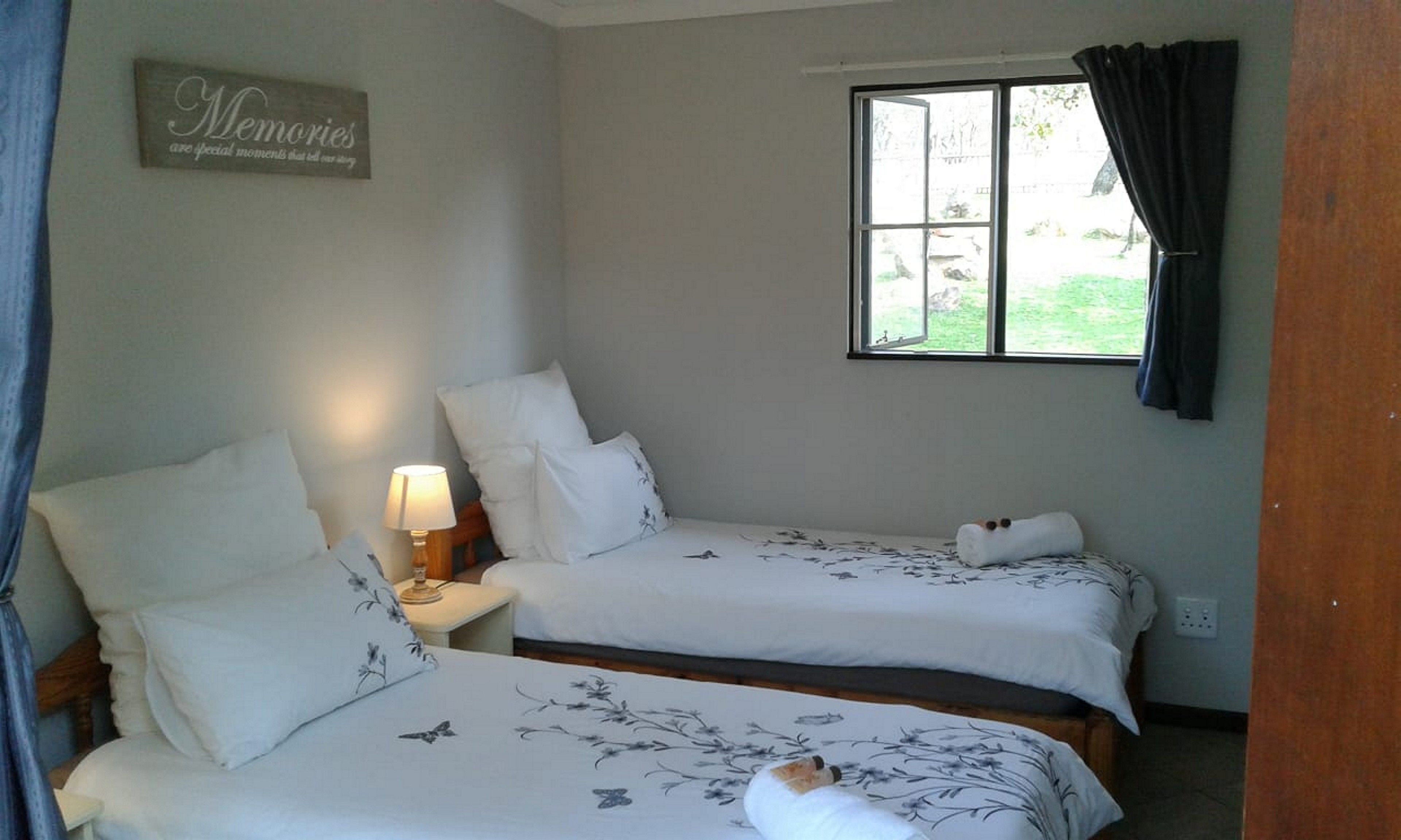 A bedroom with two beds, a bedside lamp, a window with curtains, and a wall sign.