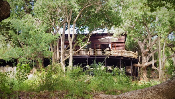 Een houten vakantiehuis met terras, omringd door bomen en een rivier.