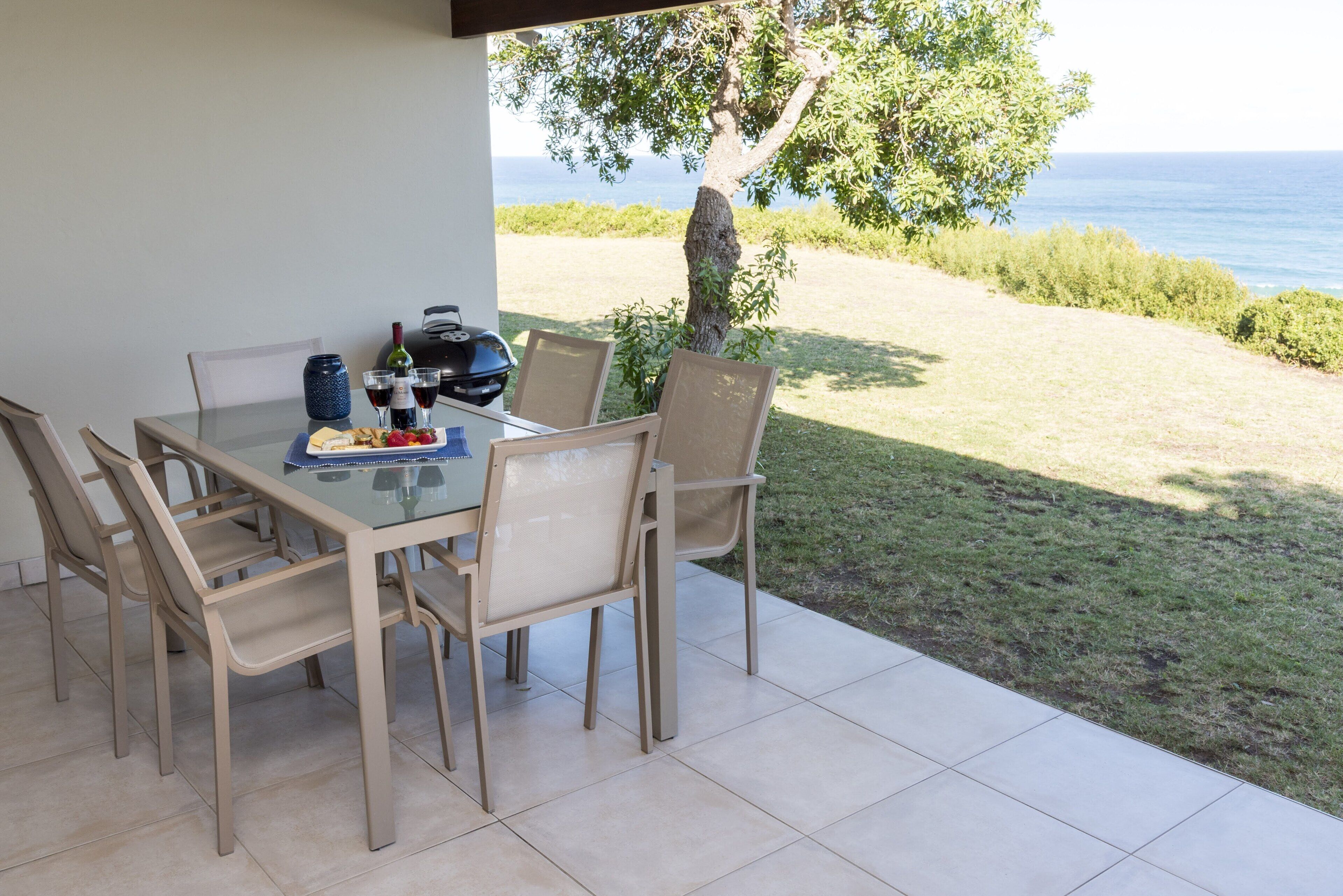 Ein Esstisch mit Stühlen, einer Weinflasche und einem Notizbuch auf einer Terrasse mit Blick aufs Meer.
