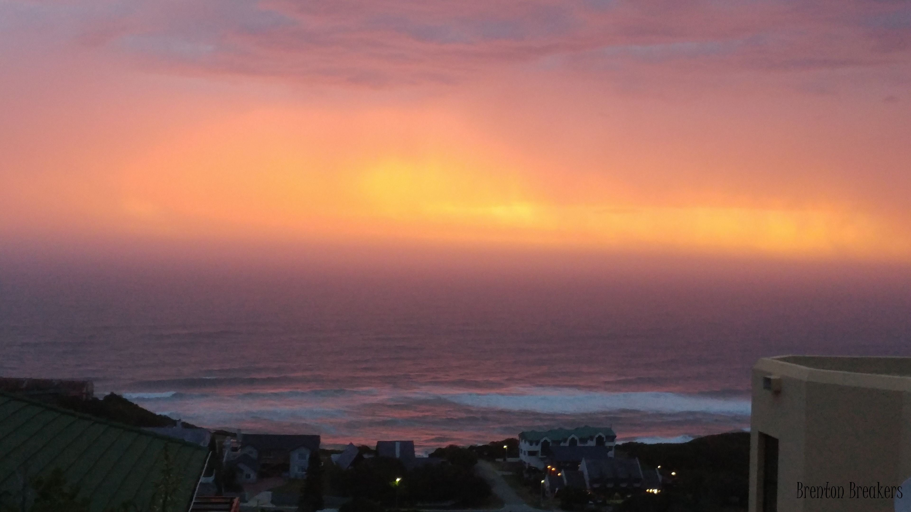 A coastal sunset view with buildings in the foreground.
