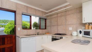 Una cocina moderna con armarios blancos, lavavajillas integrado, estufa y microondas.
