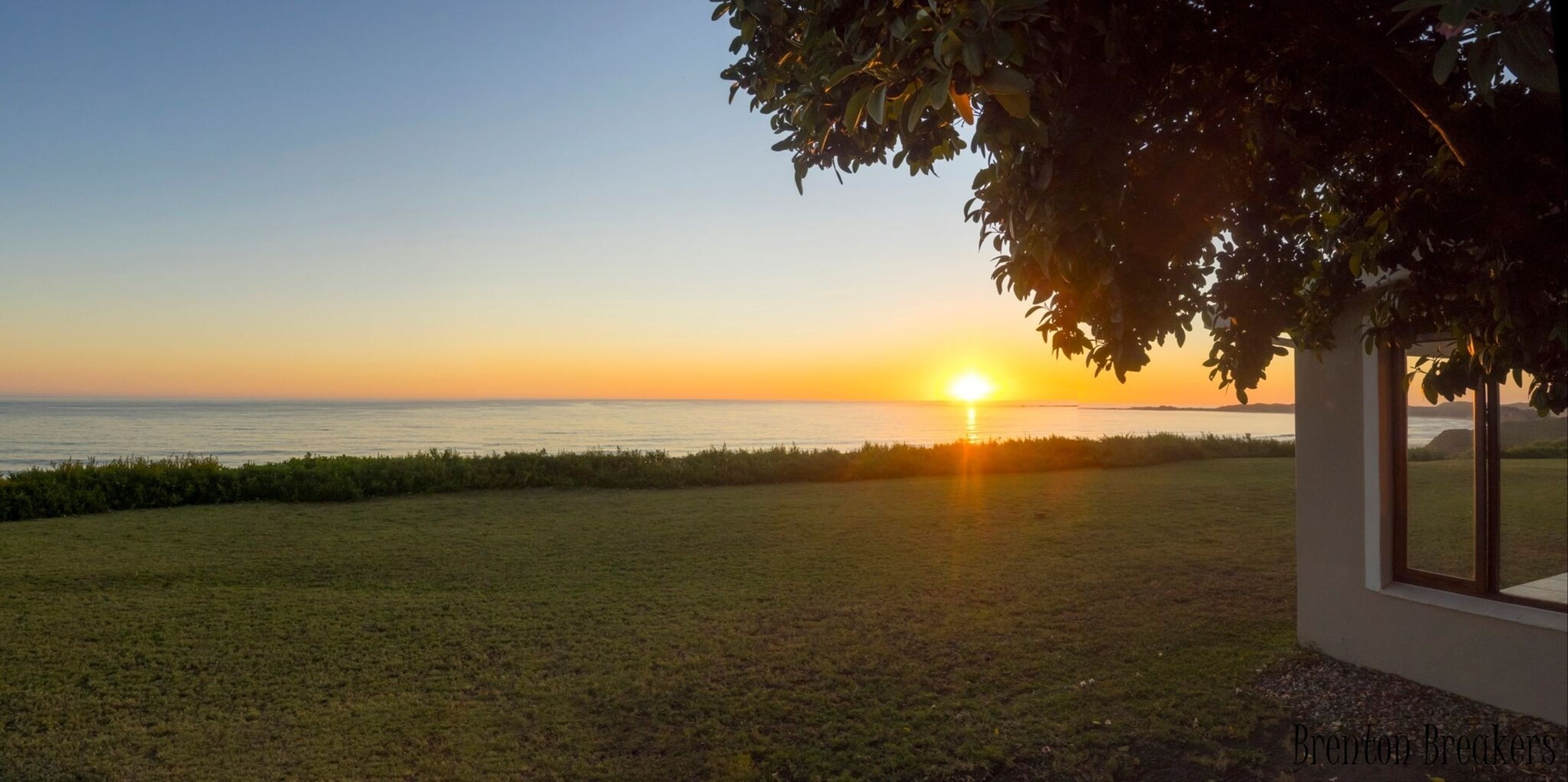 A sunset over a grassy field with a building in the foreground.
