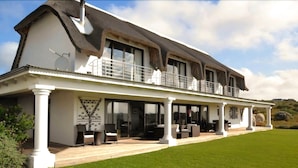 Une grande maison à deux étages, dotée d’un balcon, d’une terrasse couverte et d’une pelouse bien entretenue.