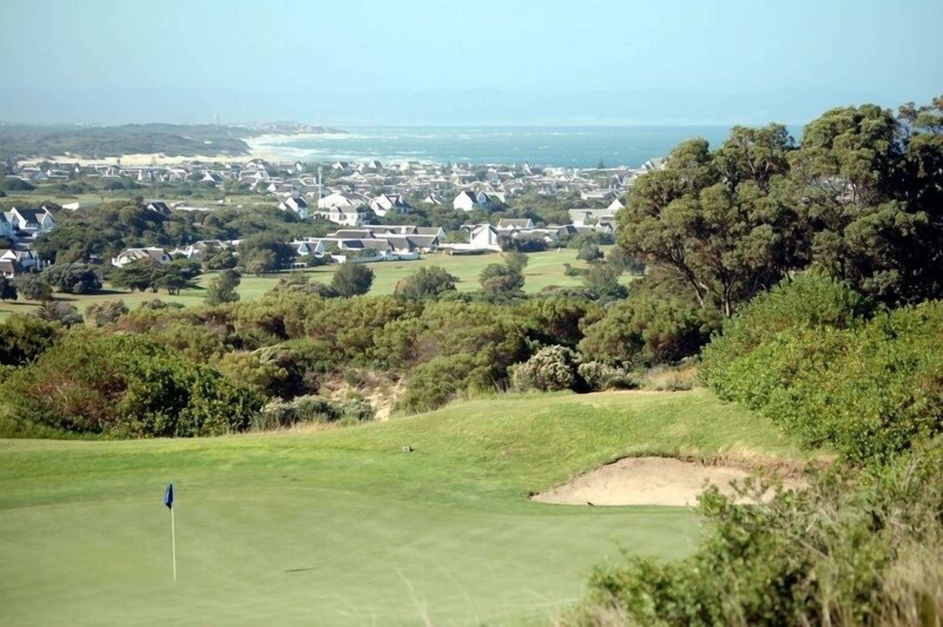 Un campo de golf con una bandera, rodeado de viviendas y abundante vegetación.