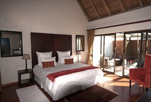Um quarto espaçoso com uma cama grande, uma mesinha de cabeceira, uma cadeira vermelha e uma porta de vidro corrediça para uma varanda.