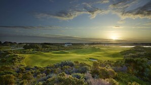 Un terrain de golf avec un club-house et un coucher de soleil en arrière-plan.