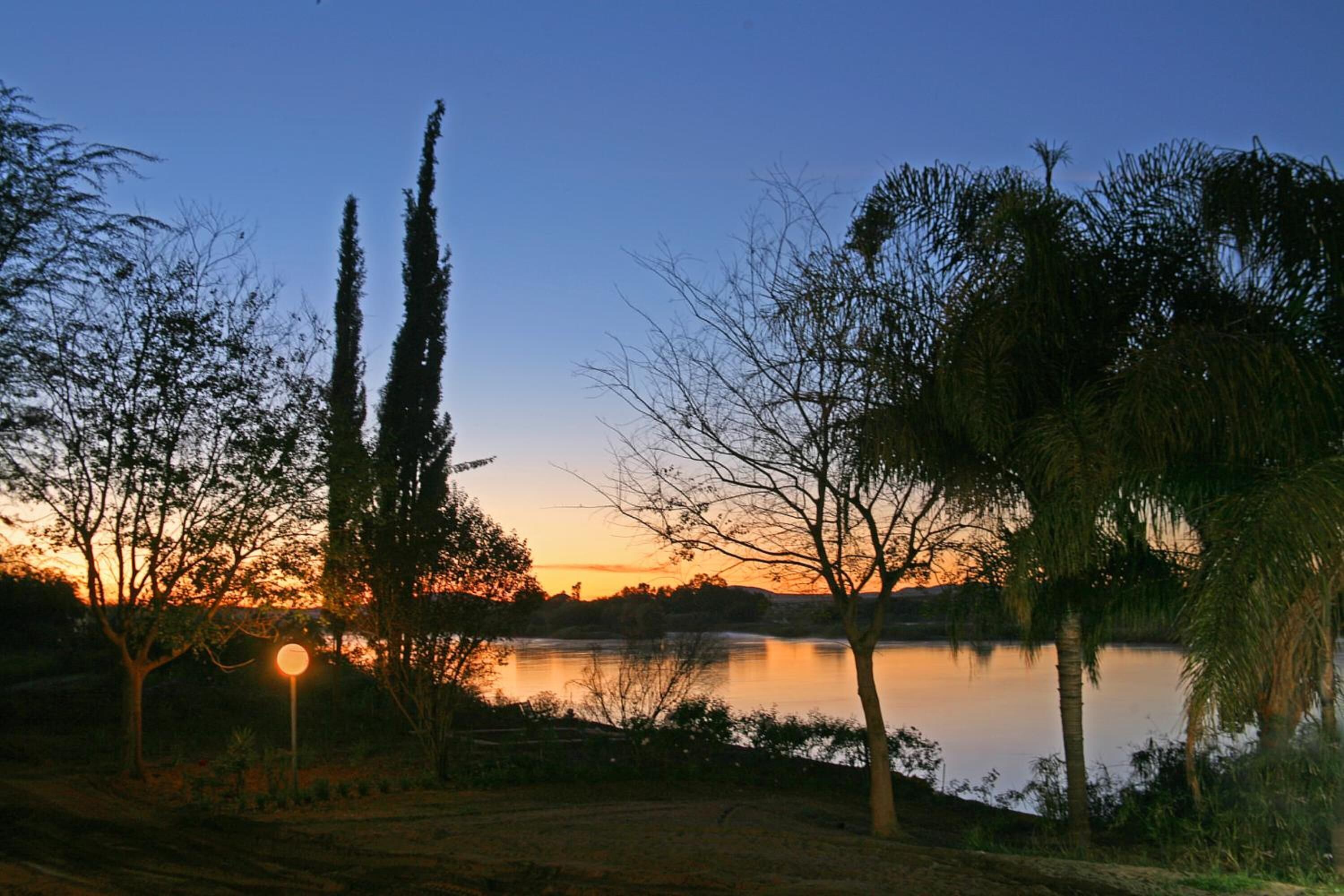 A serene lakeside view with trees and a clear sky at dusk.