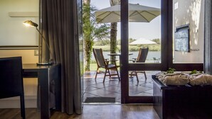 Habitación con escritorio, silla y vista a un patio al aire libre con sillas y sombrillas.