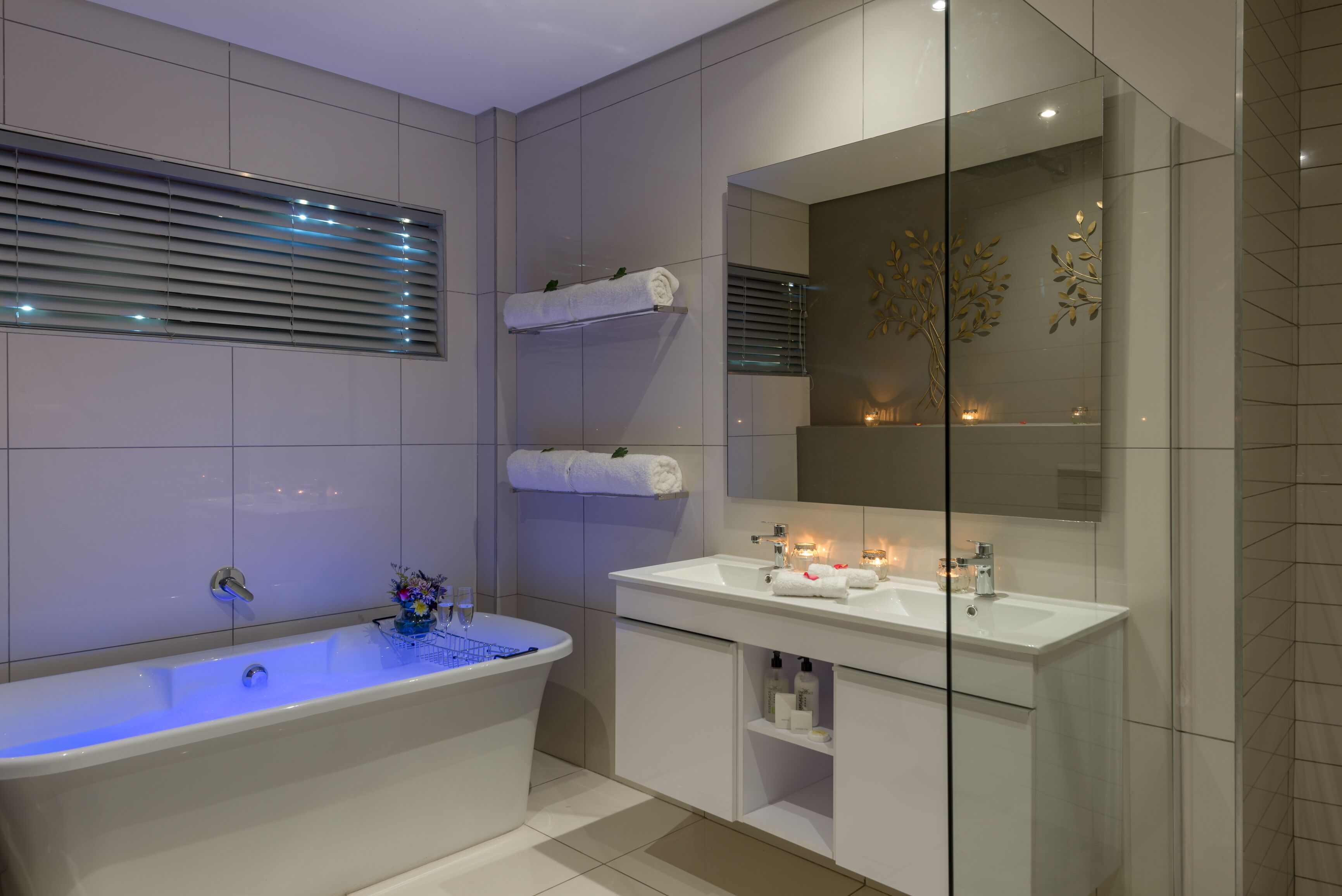 A modern bathroom with a freestanding bathtub, a vanity with a mirror, and a shelf with towels.