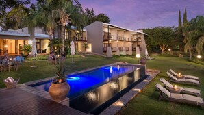Un área de piscina con sillones de descanso, un césped cuidado y un edificio con varios balcones.