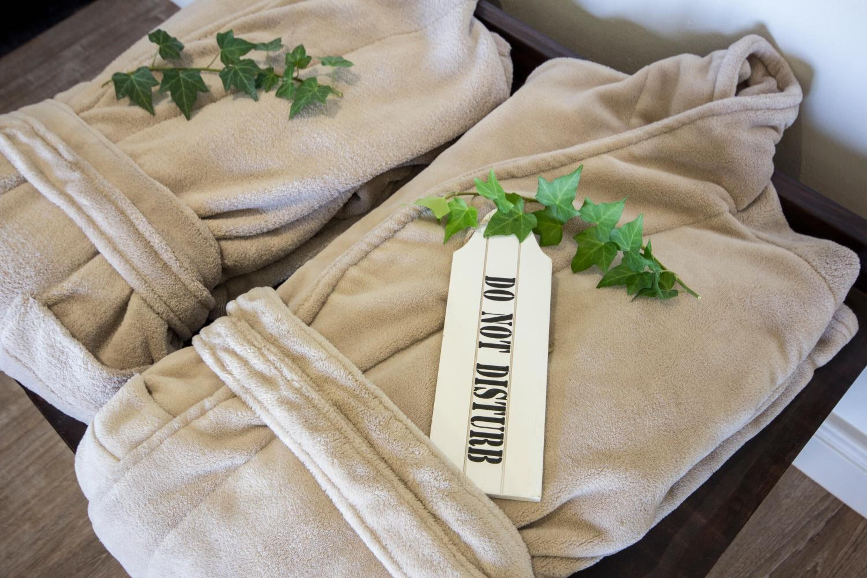 Two beige towels with a 'DO NOT DISTURB' sign and green leaves on a wooden surface.