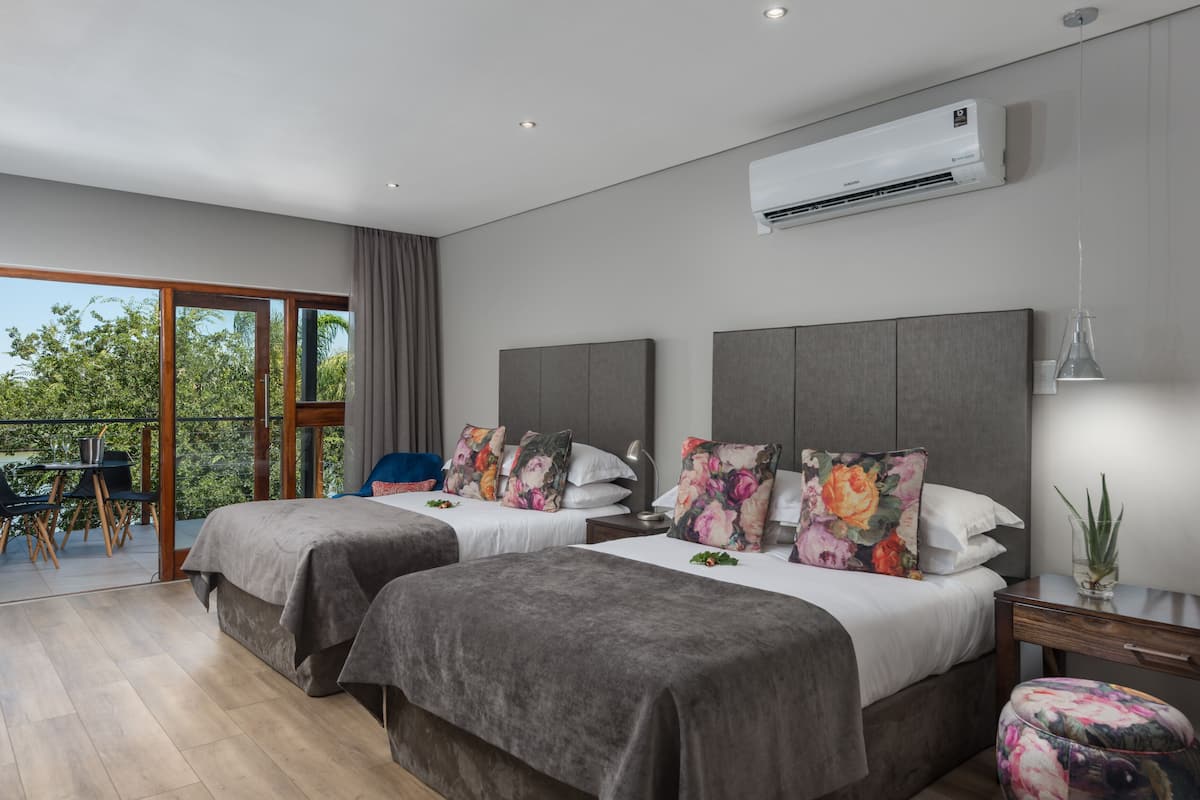 A modern hotel room with two beds, a balcony, and an air conditioning unit.