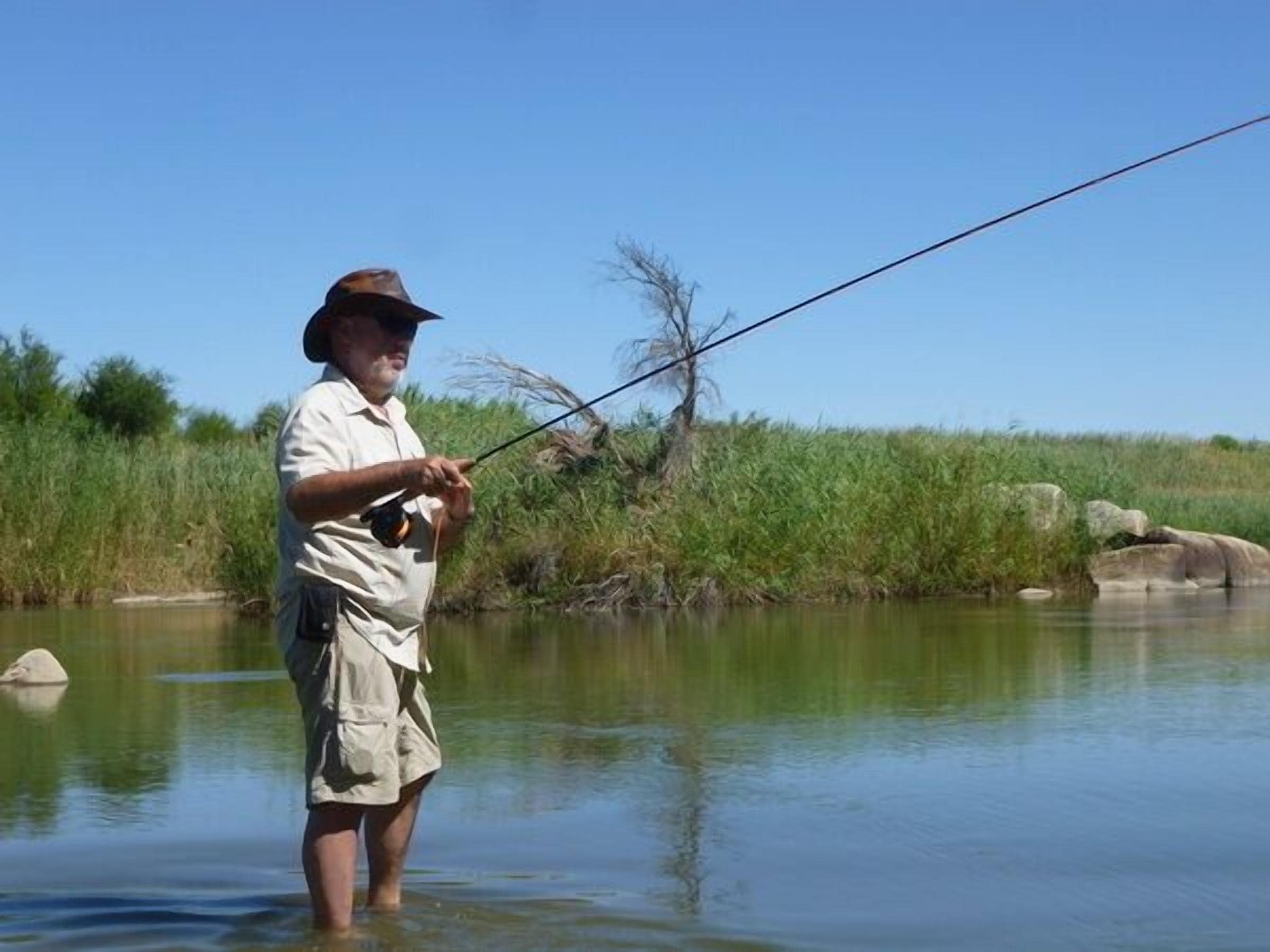 A person fishing in a calm river surrounded by greenery.