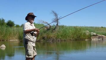 A person fishing in a calm river surrounded by greenery.