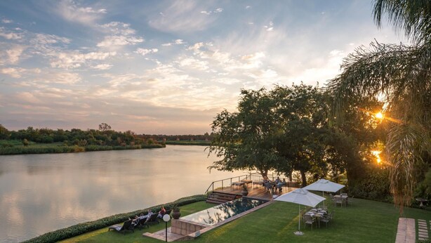Un entorno tranquilo junto al lago, con una terraza con vistas al agua, rodeado de exuberante vegetación y un cielo despejado.