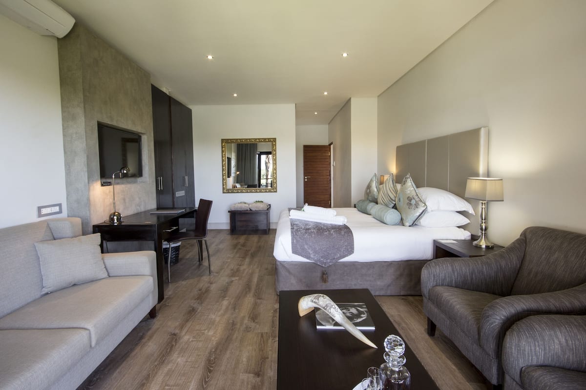 A modern hotel room with a bed, two sofas, a desk, and a large mirror.