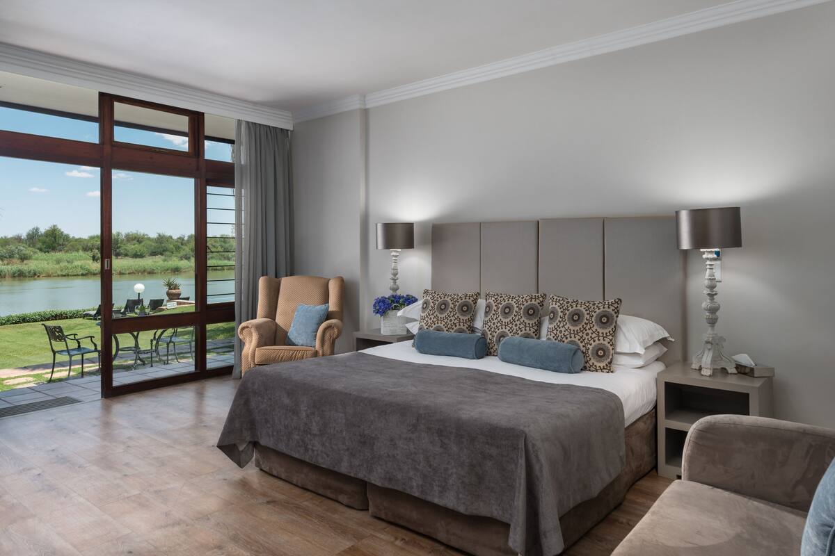 A bedroom with a large bed, two nightstands, a chair, and a view of a lake through a glass door.